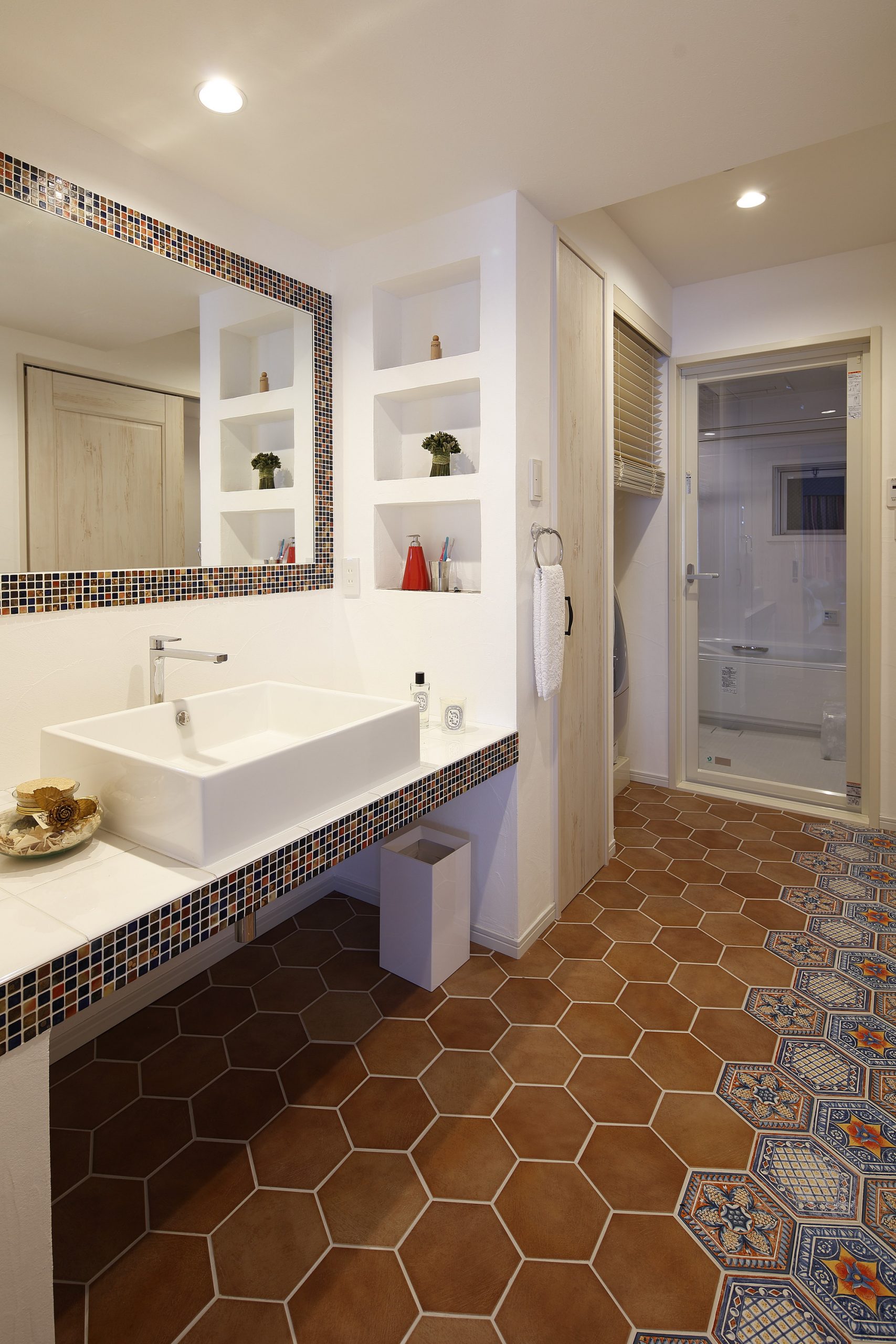 洗面台の写真。洗面台とミラー周りと、床のタイルにもこだわり、オレンジとブルーを基調とした楽しい空間となっている。