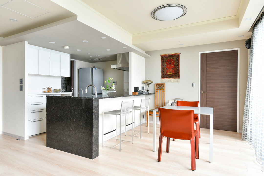 ダイニングキッチンの写真。ホワイトをベースにした空間に、キッチン天板に使用した御影石のブラックと、ダイニングチェアのレッドが映える。