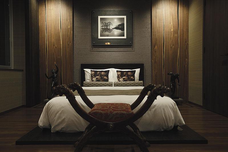 マンションリノベーション後、ダークカラーを基調としアートやオットマンを配置したホテルライクな寝室画像